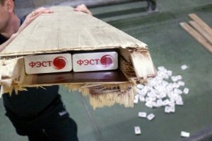 Funkcjonariusz trzyma deskę z widoczną skrytką, w której znajdują się papierosy